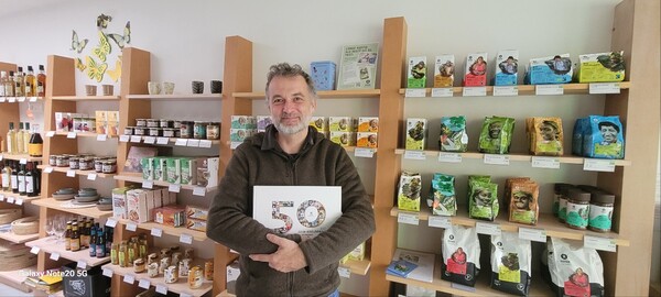 ▲ 공정무역 제품과 로컬페어트레이드 제품 앞에서 개업 50주년 기념 발간도서(2023)를 들고 있는 자원봉사자 비요른. ©최은주